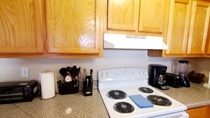 Una cucina con mobili in legno, un fornello bianco, un tostapane, una macchina per il caffè e diversi utensili.