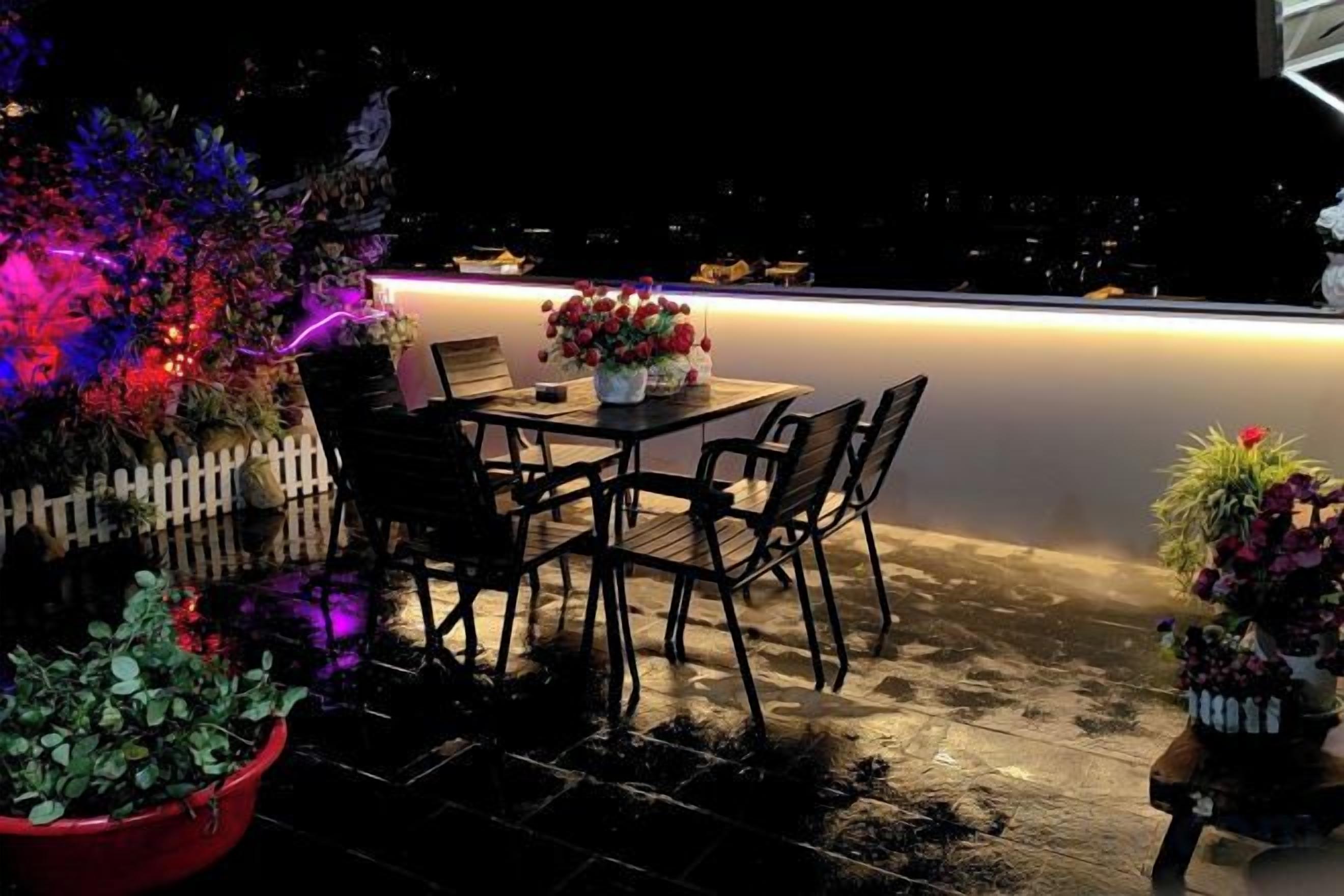 Un patio al aire libre con mesa y sillas, cerca de un seto blanco y plantas en macetas.