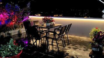Un patio al aire libre con mesa y sillas, cerca de un seto blanco y plantas en macetas.