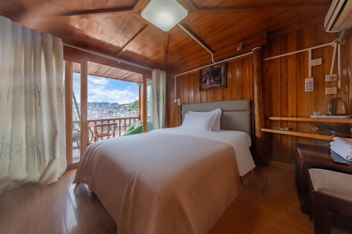 A wooden room with a bed, a desk, and a view of a cityscape through a large window.