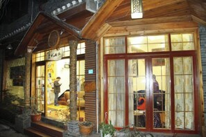 A traditional wooden building with a large glass door and windows, a wooden porch with potted plants, and a sign above the entrance. - Biancheng Shanshui Inn (Fenghuang County)