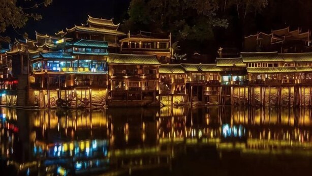Un bâtiment traditionnel chinois, à plusieurs niveaux, dont l’image se reflète dans l’eau.