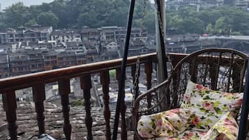 Una silla de mimbre con cojines florales en un balcón con vista a un pueblo tradicional de edificios escalonados y un puente.