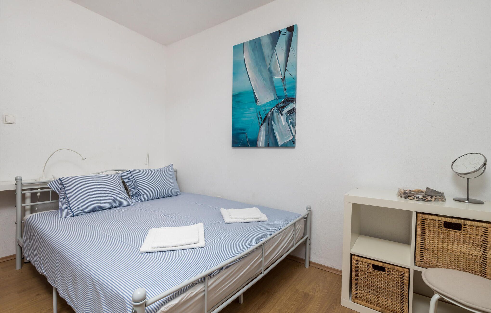Quarto com cama, almofadas, quadro, mesa de cabeceira e cestos de vime.
