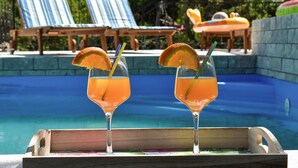 Zwei Gläser Orangensaft mit Strohhalmen und Orangenscheiben auf einem Tablett am Pool.