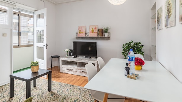 Una sala de estar moderna con un sofá blanco, una mesa de centro, un televisor de pantalla plana y un comedor con una mesa y sillas blancas.