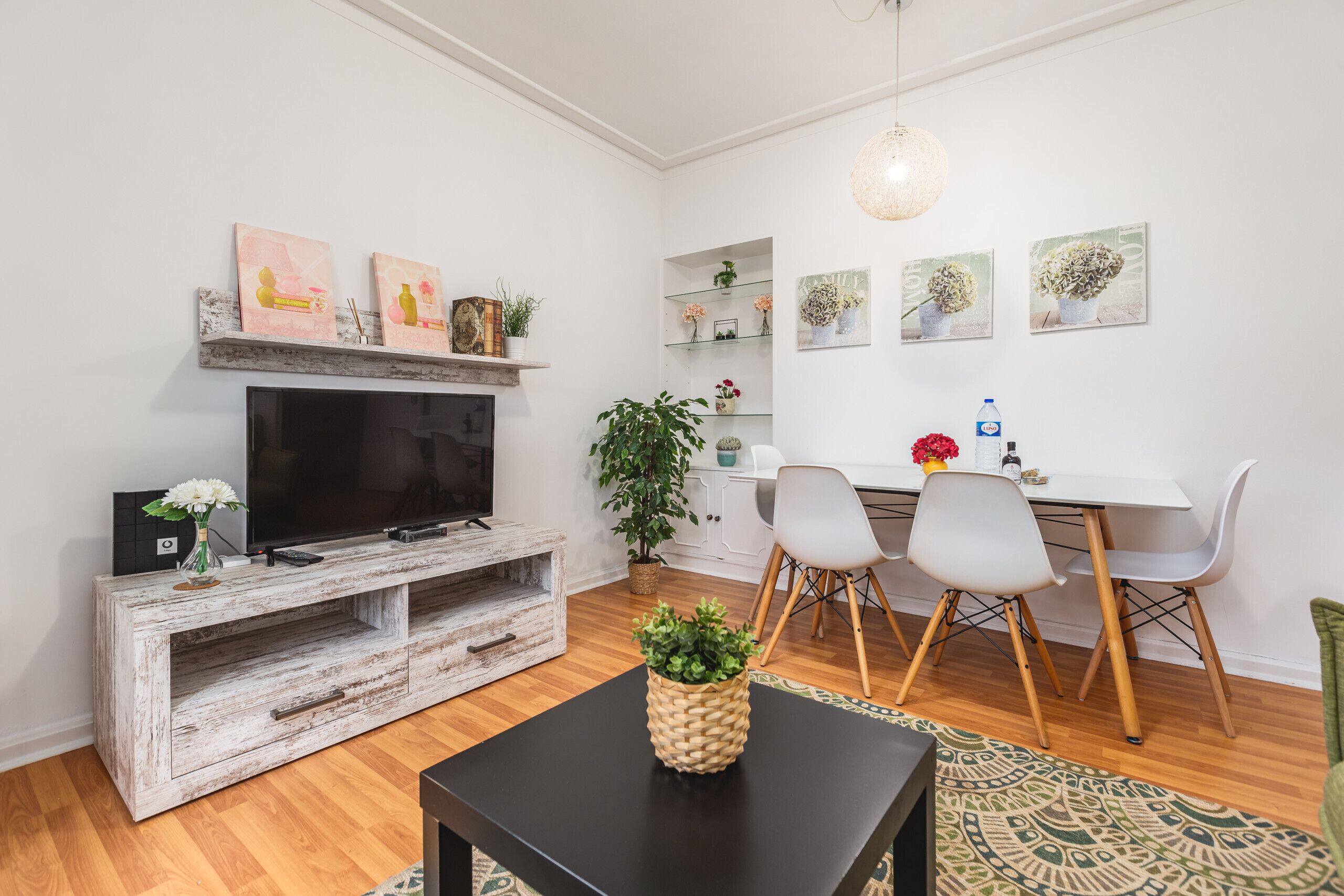 Ein modernes Wohnzimmer mit Fernseher, einer Holzunterhaltungsecke, einem Esstisch mit Stühlen und Zimmerpflanzen.