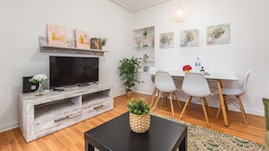 Una sala de estar moderna con televisor, mueble de madera para entretenimiento, mesa de comedor con sillas y plantas decorativas.