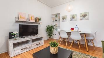 Un salon moderne comprenant un téléviseur, un meuble de rangement en bois, une table à manger avec des chaises et des plantes décoratives.