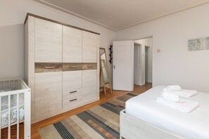 Une chambre à coucher comprenant un lit, une armoire, un berceau et une porte donnant sur une autre pièce.