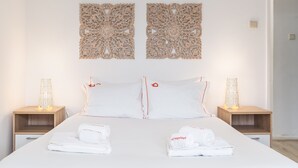 Habitación de hotel con una cama, dos mesitas de noche, dos paneles decorativos en la pared y dos toallas dobladas con un logotipo.