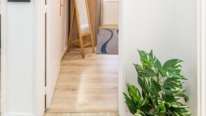 Un pasillo con piso de madera, un espejo de pie y una planta en maceta.