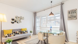 Una sala de estar moderna con una mesa de comedor de cristal, un sofá con cojines estampados, una lámpara de pie y un letrero motivacional en la pared.