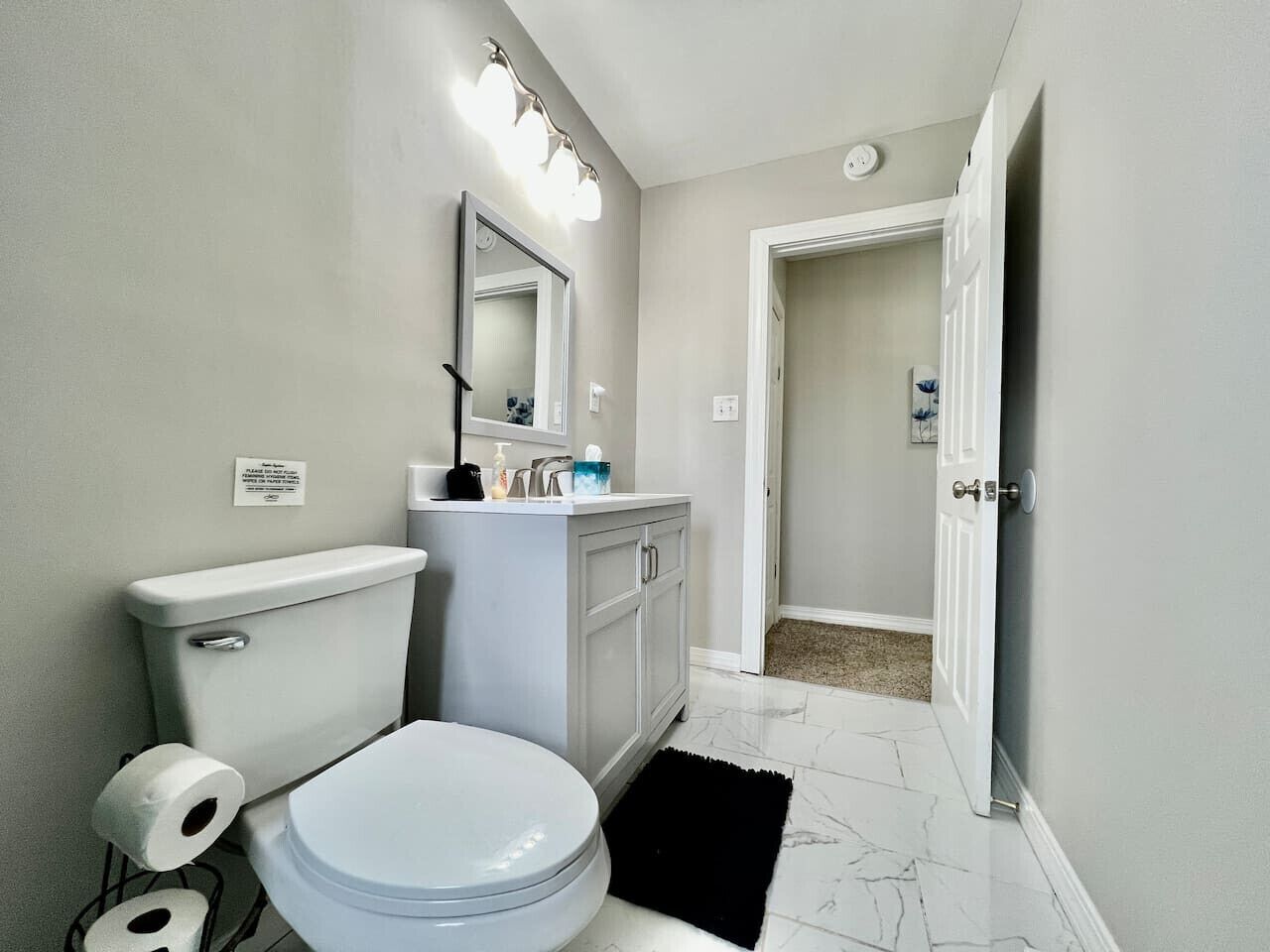 Une salle de bain avec des toilettes, un lavabo, un miroir et un tapis noir.