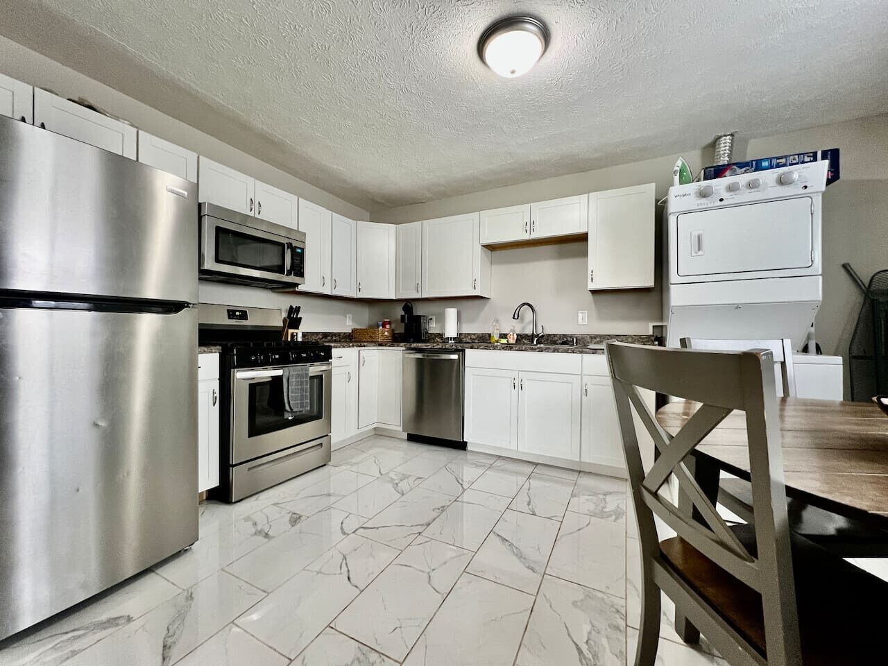 A modern kitchen with stainless steel appliances, white cabinets, and a marble floor.