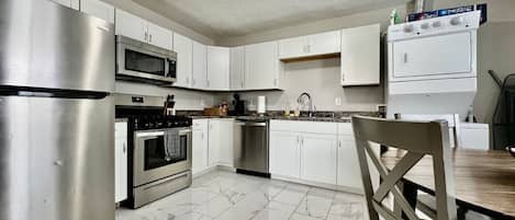 A modern kitchen with stainless steel appliances, white cabinets, and a marble floor.