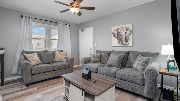 A living room with two grey sofas, a wooden coffee table, a ceiling fan, and a window with curtains.