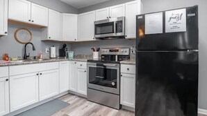 A modern kitchen with white cabinets, stainless steel appliances, and a black refrigerator. - 17 S First - Unit 6 · 17 s first street unit 6 (Trenton)