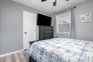 Ein Schlafzimmer mit einem Bett, einem Schminktisch, einem Fernseher und einem Deckenventilator.