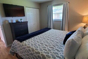 A bedroom with a bed, a dresser, a television, a window with curtains, and a lamp.
