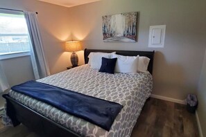 Un lit bien fait, avec une couvre-lit à motifs, une lampe de chevet et un tableau accroché au mur.