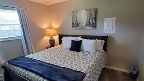 A neatly made bed with a patterned bedspread and pillows, a bedside lamp, and a painting on the wall.