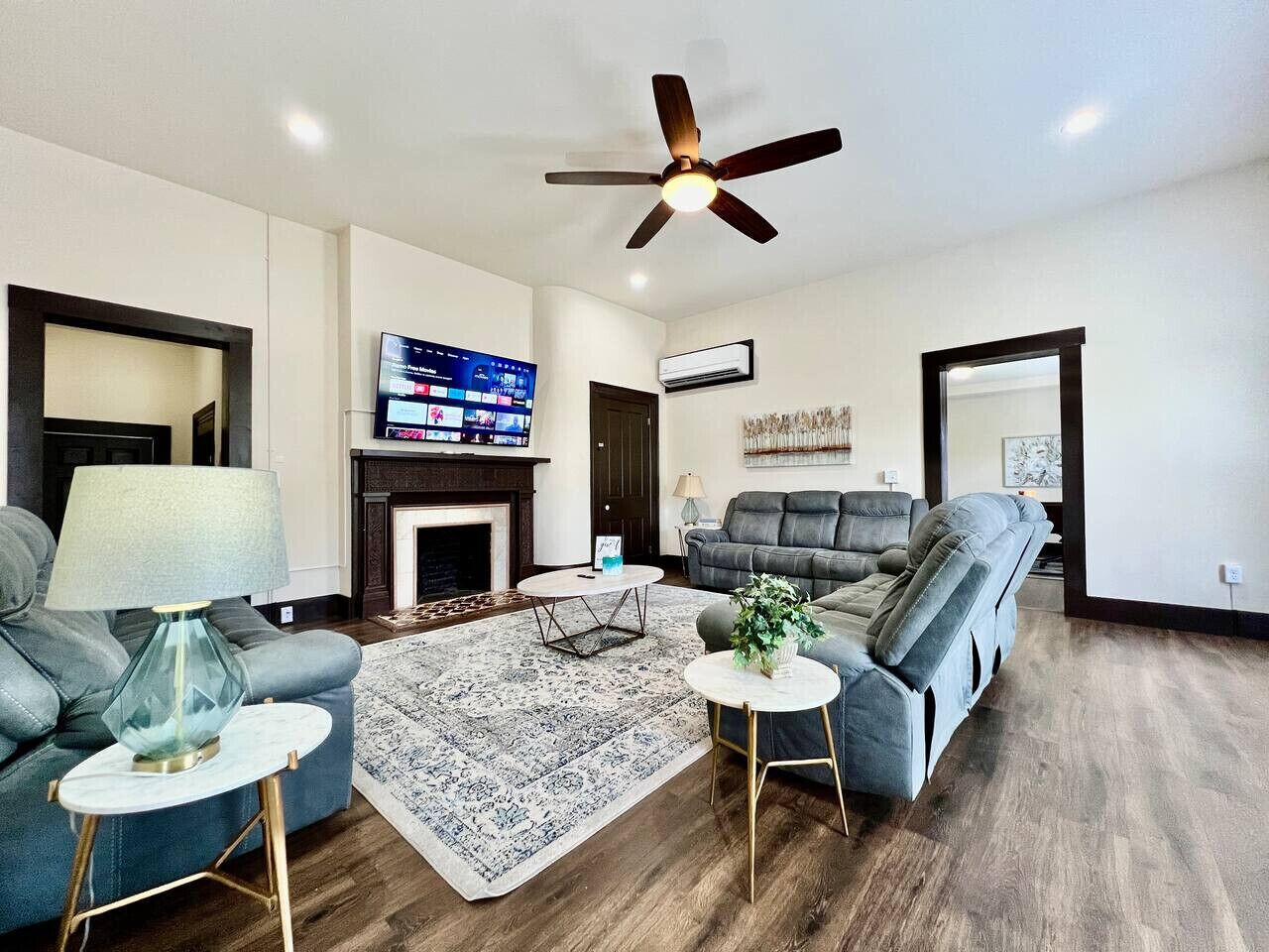 A modern living room with a fireplace, a ceiling fan, and a flat-screen TV mounted on the wall.