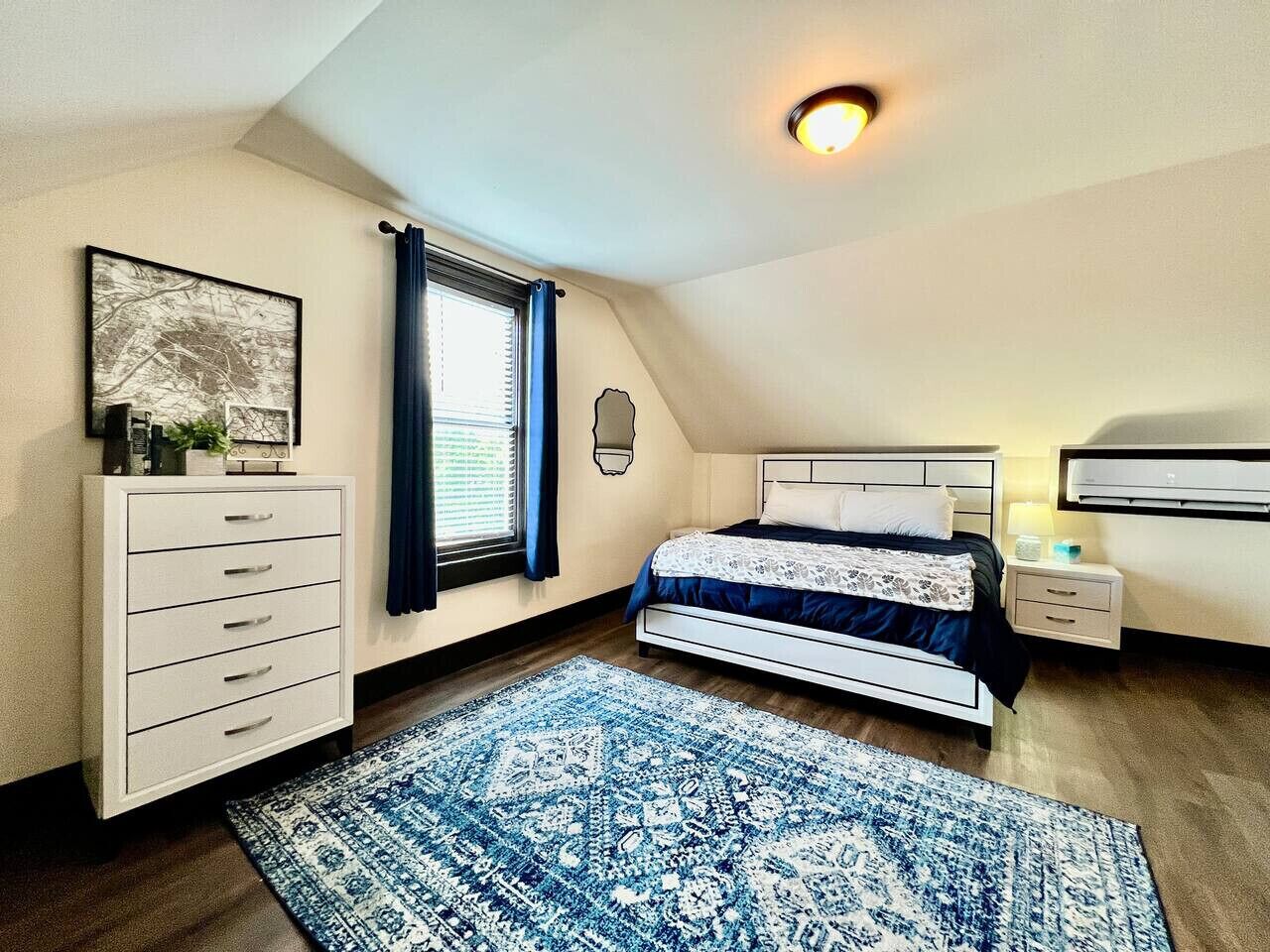 A bedroom with a bed, bedside table, dresser, and a window with curtains.