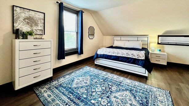 Un dormitorio con cama, mesita de noche, cómoda y ventana con cortinas.