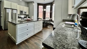 Una cocina moderna con armarios blancos, encimera de granito, electrodomésticos de acero inoxidable y un comedor con mesa y sillas.