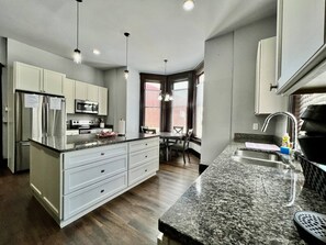 A modern kitchen with white cabinets, a granite countertop, stainless steel appliances, and a dining area with a table and chairs. - Newly Renovated Historic mansion 8 Bedrooms (Hamilton)