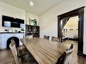 A dining room with a long wooden table, chairs, a fireplace, a television, and a bookshelf.