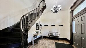 Una escalera con barandilla negra, un candelabro, un radiador y una puerta.