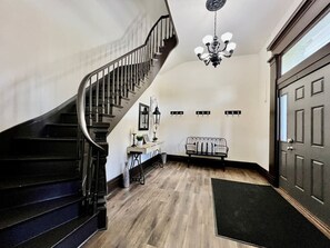 A staircase with a black railing, a chandelier, a radiator, and a door. - Newly Renovated Historic mansion 8 Bedrooms (Hamilton)