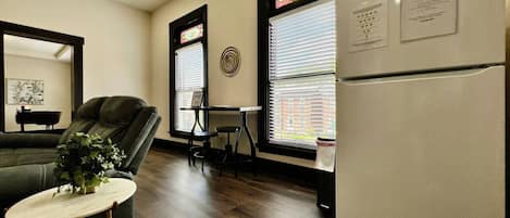 Un espacio habitable compacto con sofá, una mesita redonda, refrigerador y ventana con persianas.