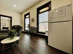 A compact living space with a sofa, a small round table, a refrigerator, and a window with blinds. - Newly Renovated Historic mansion 8 Bedrooms (Hamilton)
