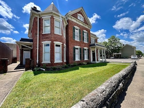 A two-story brick house with a front porch, a stone retaining wall, and a well-maintained lawn.