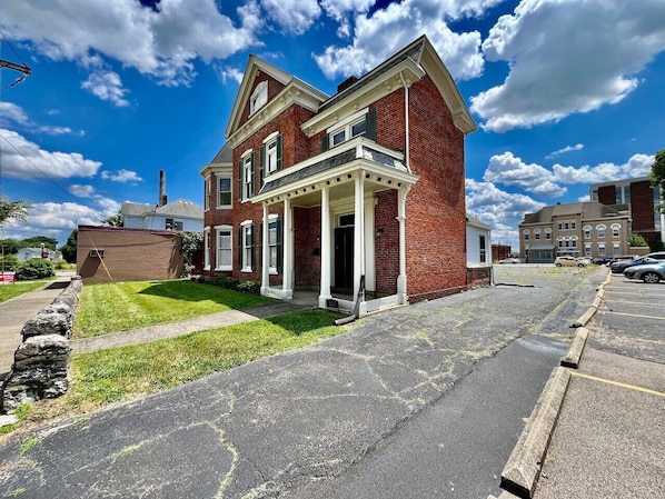 A two-story brick house with a front porch, a stone wall, and a parking lot.