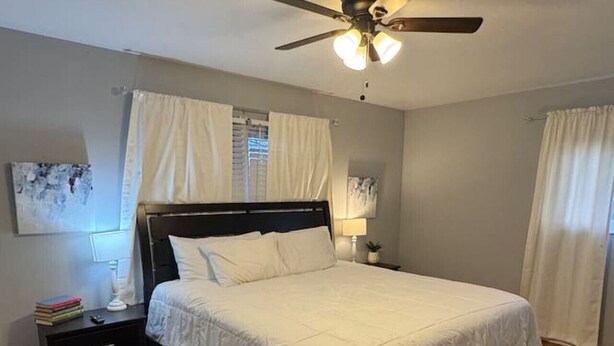 Un dormitorio con cama, mesita de noche, ventilador de techo y alfombra estampada.
