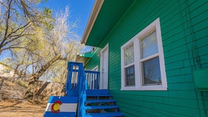A green house with a blue staircase and a Colorado state flag.