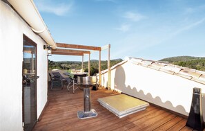 Une terrasse en bois avec un barbecue, des chaises et une table, offrant une vue sur un paysage vallonné.