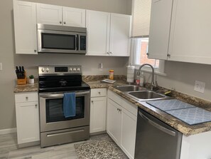 Una cocina con armarios blancos, electrodomésticos de acero inoxidable, encimera de granito y alfombra estampada.