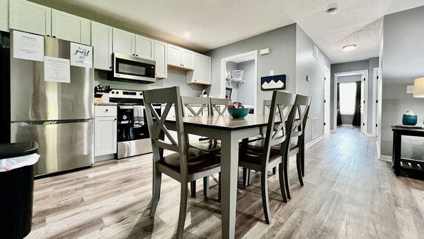 Cocina moderna con armarios blancos, electrodomésticos de acero inoxidable y un comedor con mesa y sillas de madera.
