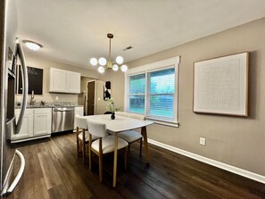 Una cocina moderna con armarios blancos, electrodomésticos de acero inoxidable y una zona de comedor con una mesa y sillas blancas.