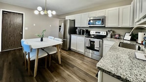 A modern kitchen with white cabinets, stainless steel appliances, a granite countertop, and a dining area with a white table and blue chairs. - 3 BDR Ranch w/ Fenced yard, laundry, garage + more (Liberty Township)