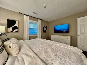Un dormitorio con cama, televisión, cómoda y ventana con cortinas.