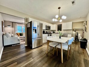 Una cocina moderna con comedor, muebles blancos, electrodomésticos de acero inoxidable y una mesa de comedor de madera.