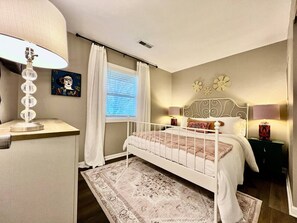 Un dormitorio con cama, mesitas de noche, lámpara, ventana con cortinas y alfombra.