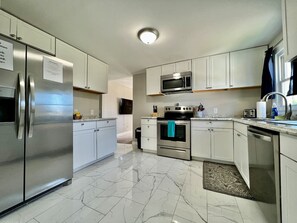 A modern kitchen with stainless steel appliances, white cabinets, and a marble floor.