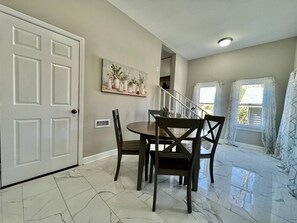 A dining area with a table and chairs, a white door, a wall-mounted plant, and a staircase leading to another room.